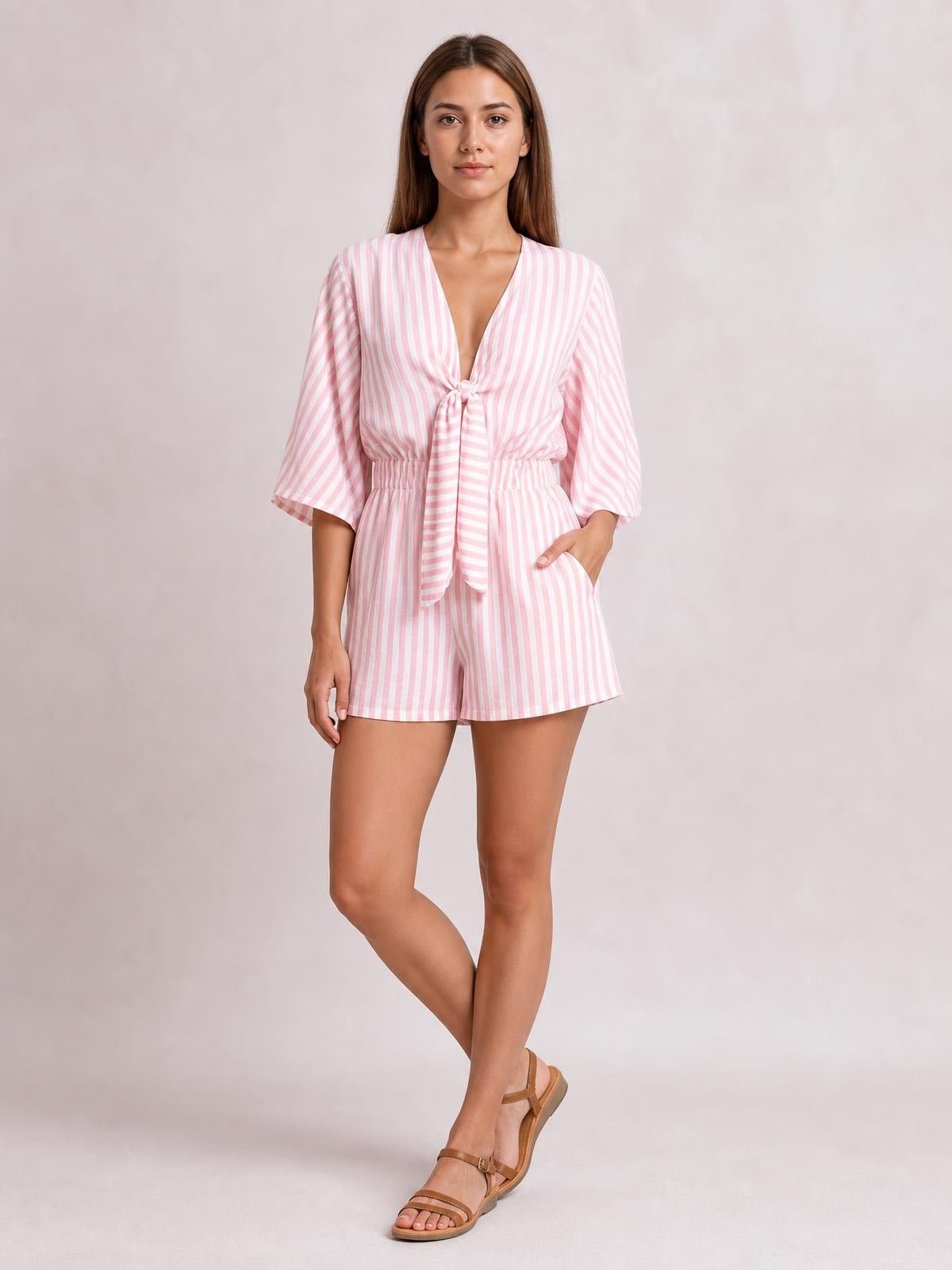 Model wearing a pink and white striped romper with kimono sleeves, a tied front bow, elastic waist, and relaxed shorts silhouette.