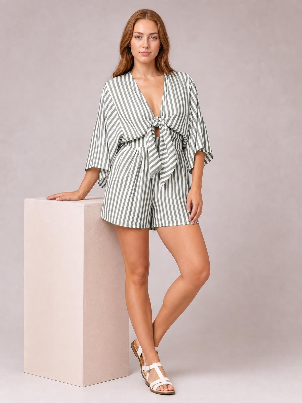 Model in a gray and white striped romper with flowing kimono sleeves, tied front bow, elastic waist, and relaxed shorts silhouette.