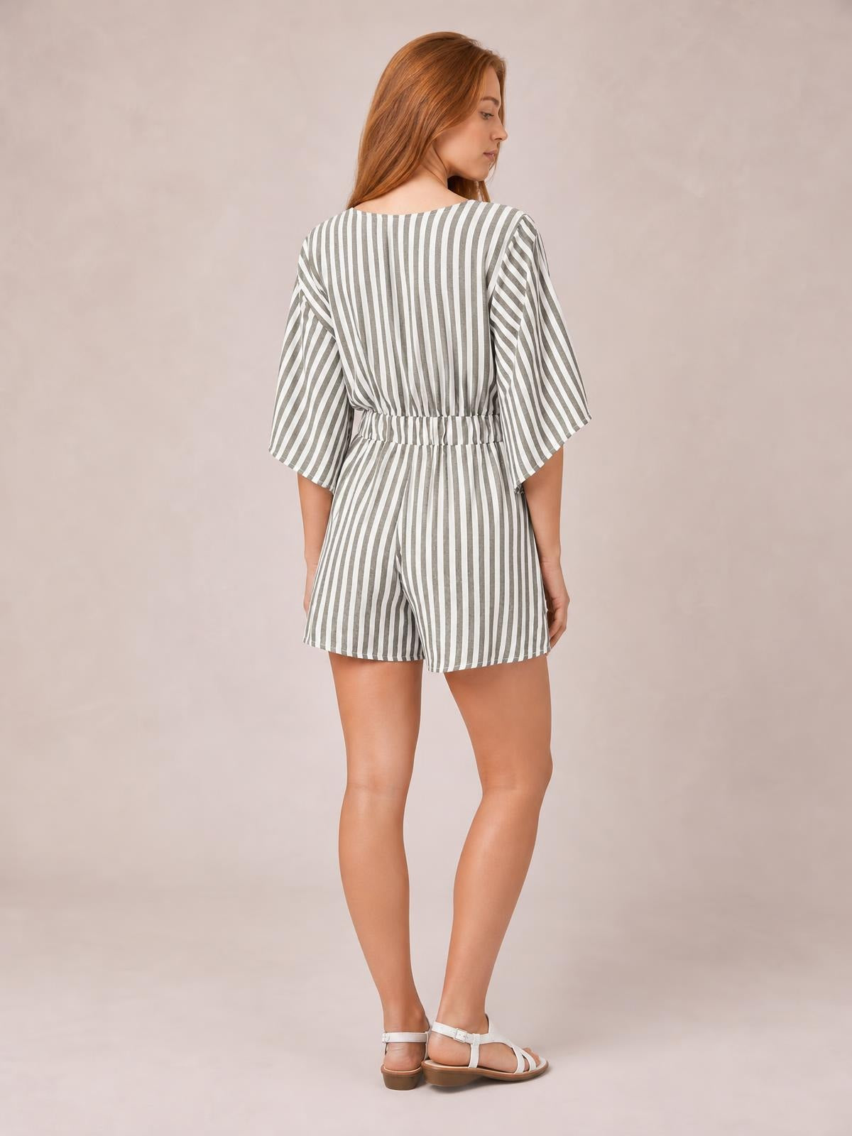 Model shown from behind in a gray-and-white striped romper with wide kimono sleeves, an elasticized waist, and relaxed shorts silhouette.