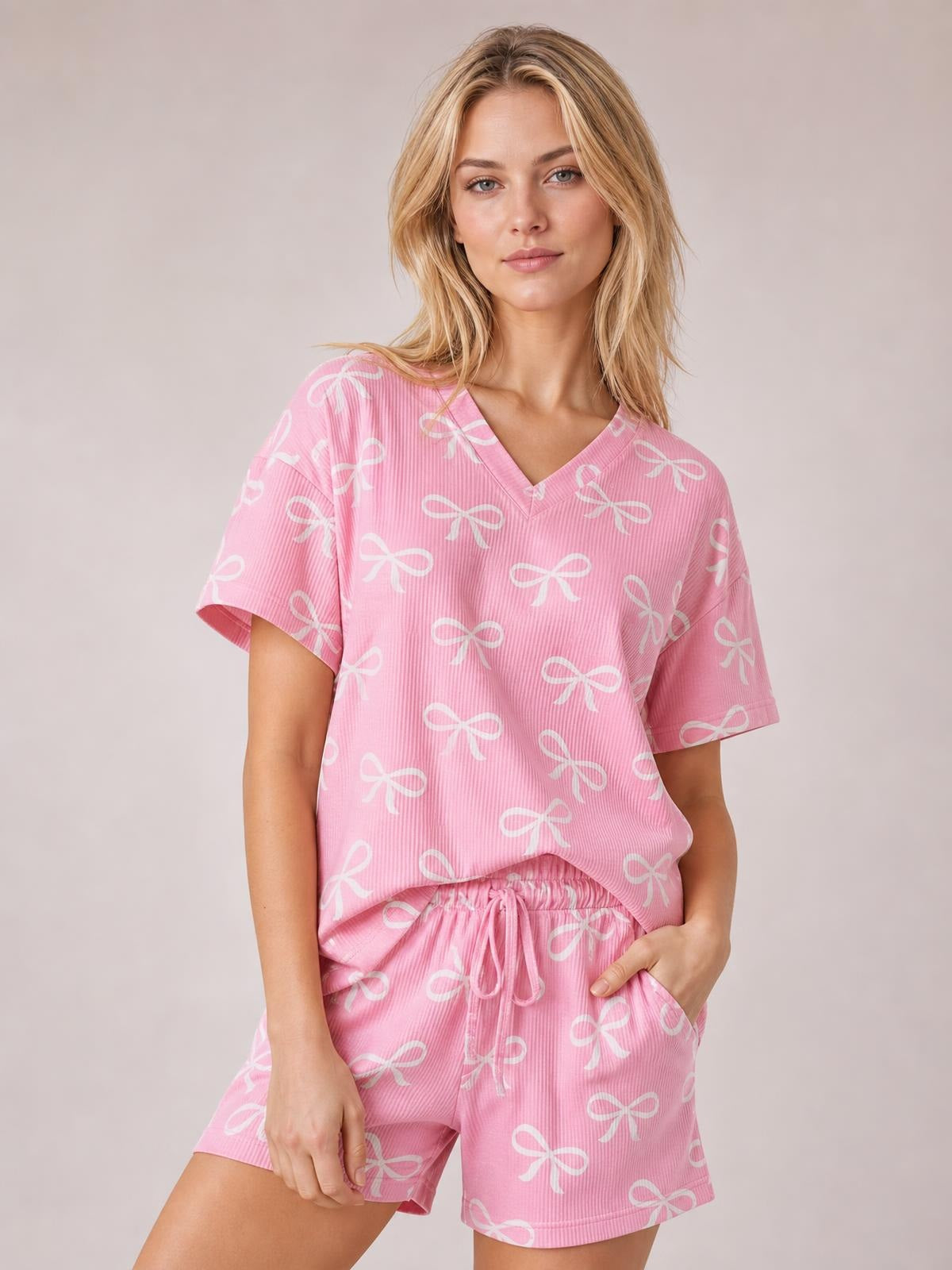 Model in a pink bowknot-print T-shirt and shorts set, featuring a notched V-neck, relaxed short sleeves, drawstring waist, and casual silhouette.