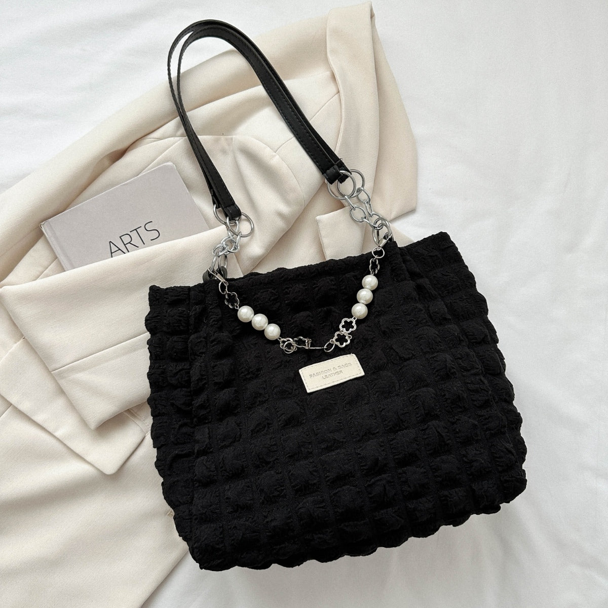 A black medium Bubble Textured Tote Bag with raised tactile texture, slender shoulder straps, linked chain accents, pearl-style strand, and front plaque.