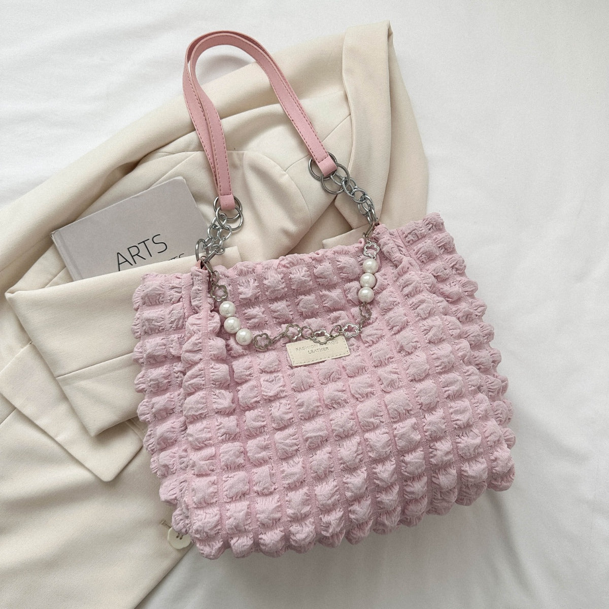 A medium pink Bubble Textured Tote Bag features a raised bubble pattern, slender shoulder straps, linked chain accents, pearl-style detailing, and a front plaque.