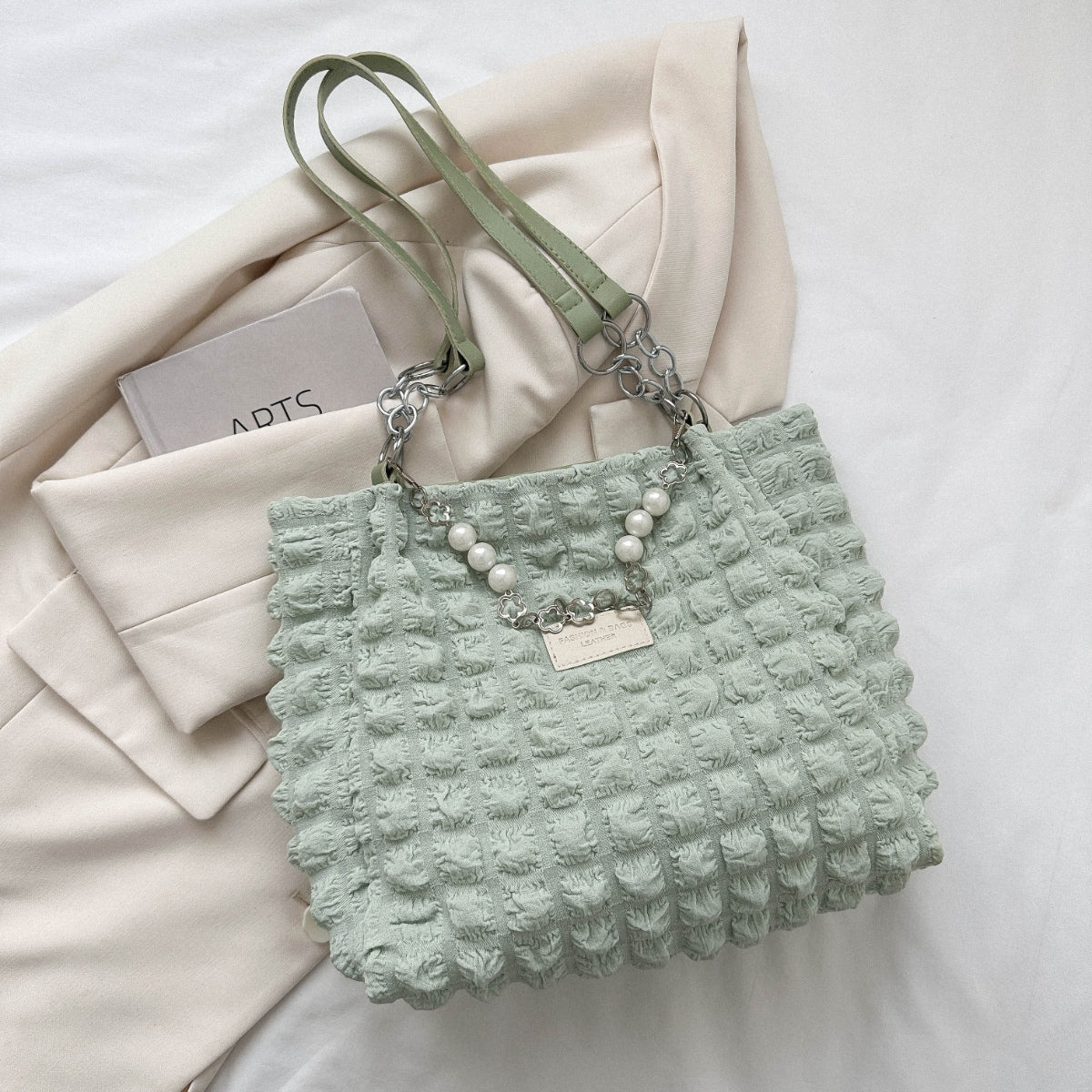 Mint green Bubble Textured Tote Bag with a raised tactile pattern, slender shoulder straps, linked chain accents, pearl-style strand, and front plaque.