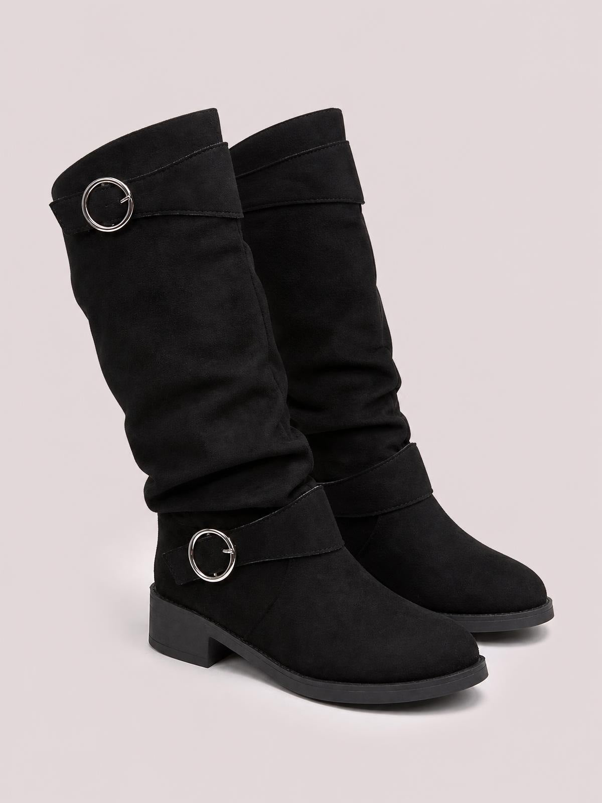 Black suede buckle accent slouch boots feature relaxed ruched shafts, wraparound straps with silver buckles, rounded toes, mid heels, and rubber soles.