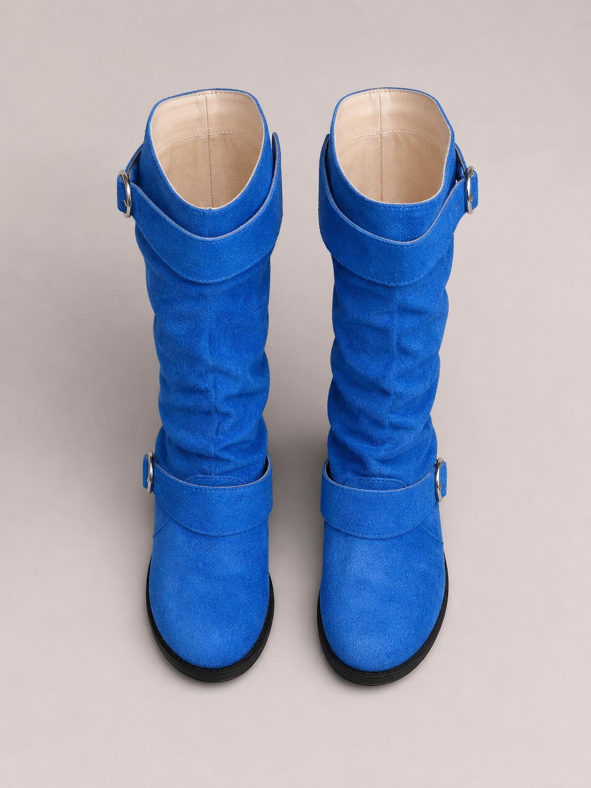 Bright blue suede slouch boots feature rounded toes, ruched shafts, wraparound buckle-accent straps, and contrasting black rubber soles.