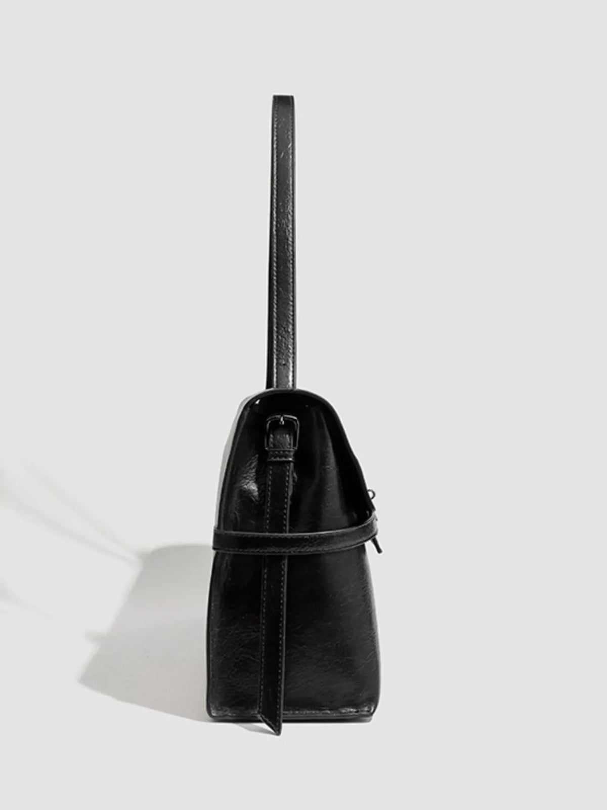 Black PU leather shoulder bag with a structured tapered silhouette, long shoulder strap, stitched panels, and a wraparound buckle strap detail.