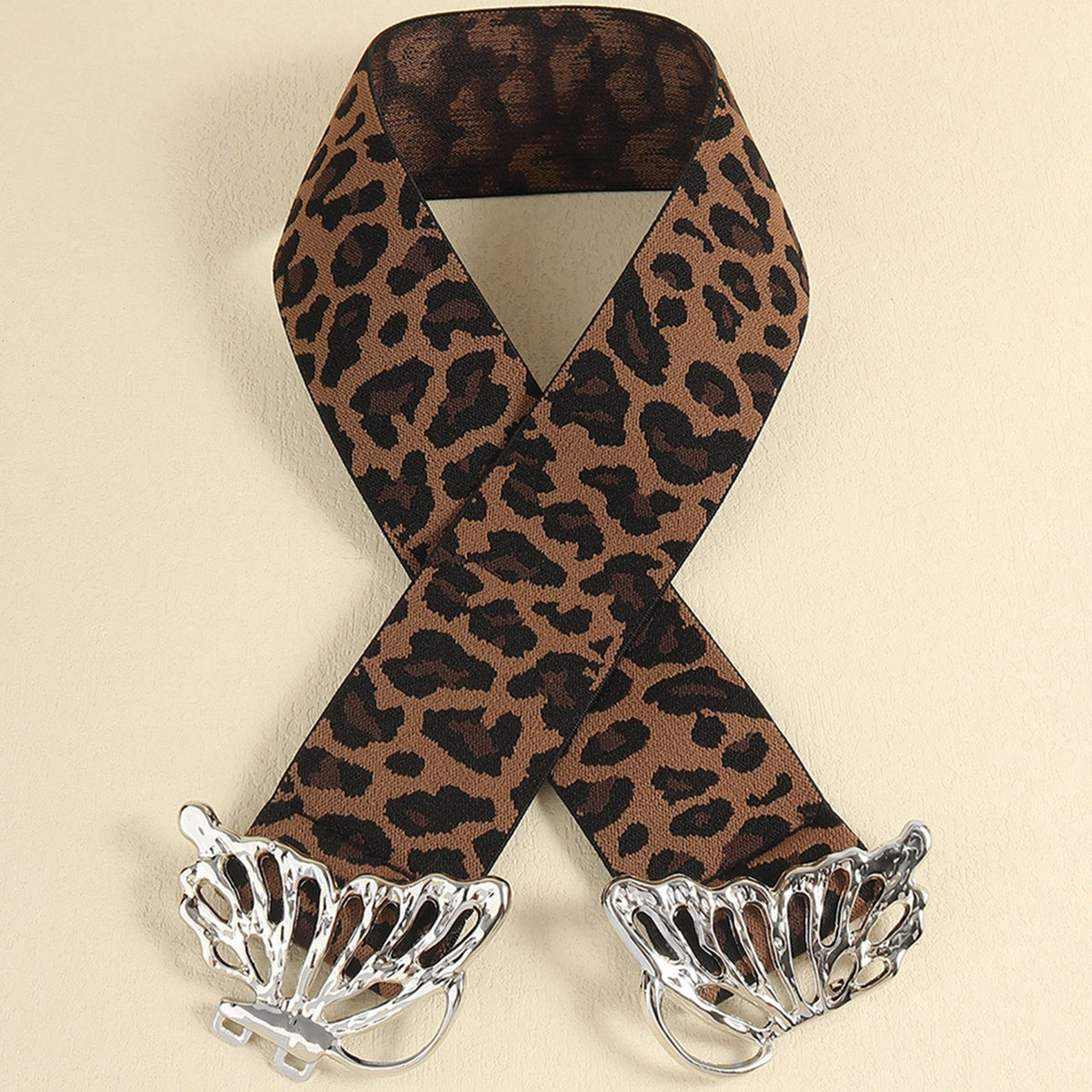 Leopard-print elastic belt with a wide, substantial band and polished silver butterfly alloy buckle displayed in a crossed flat-lay arrangement.