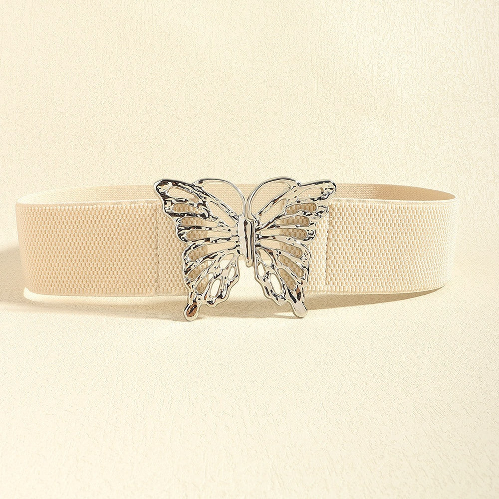 Cream elastic belt with a substantial woven band and polished butterfly alloy buckle, showcasing a feminine statement accent and defined waist silhouette.