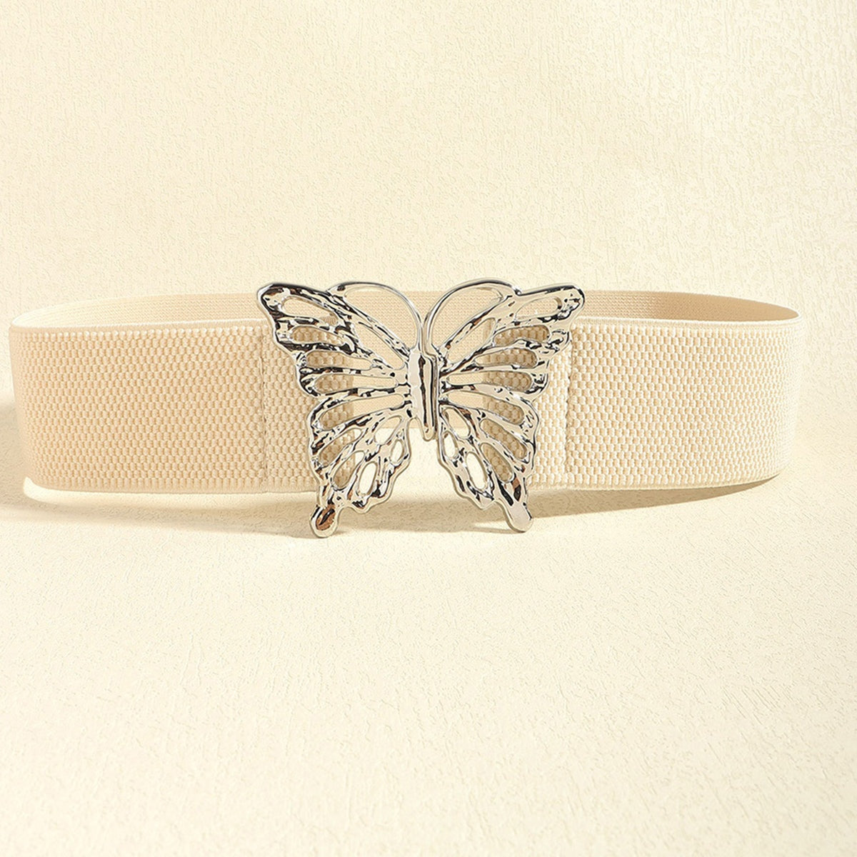 Cream elastic belt with a wide woven band and polished silver alloy butterfly buckle, creating a feminine defined waist silhouette.