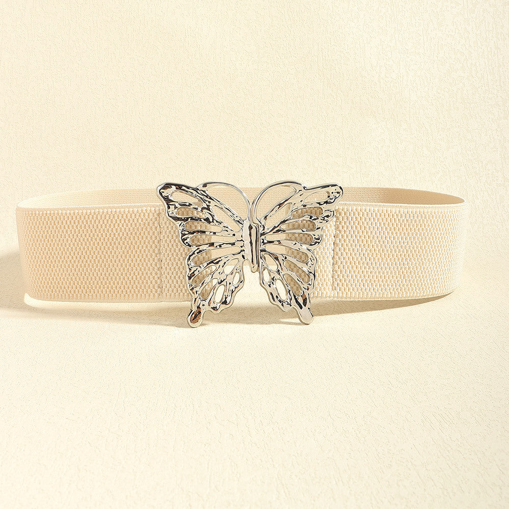 Cream elastic belt with a substantial woven band and polished butterfly alloy buckle, showcasing a feminine statement accent and defined waist silhouette.