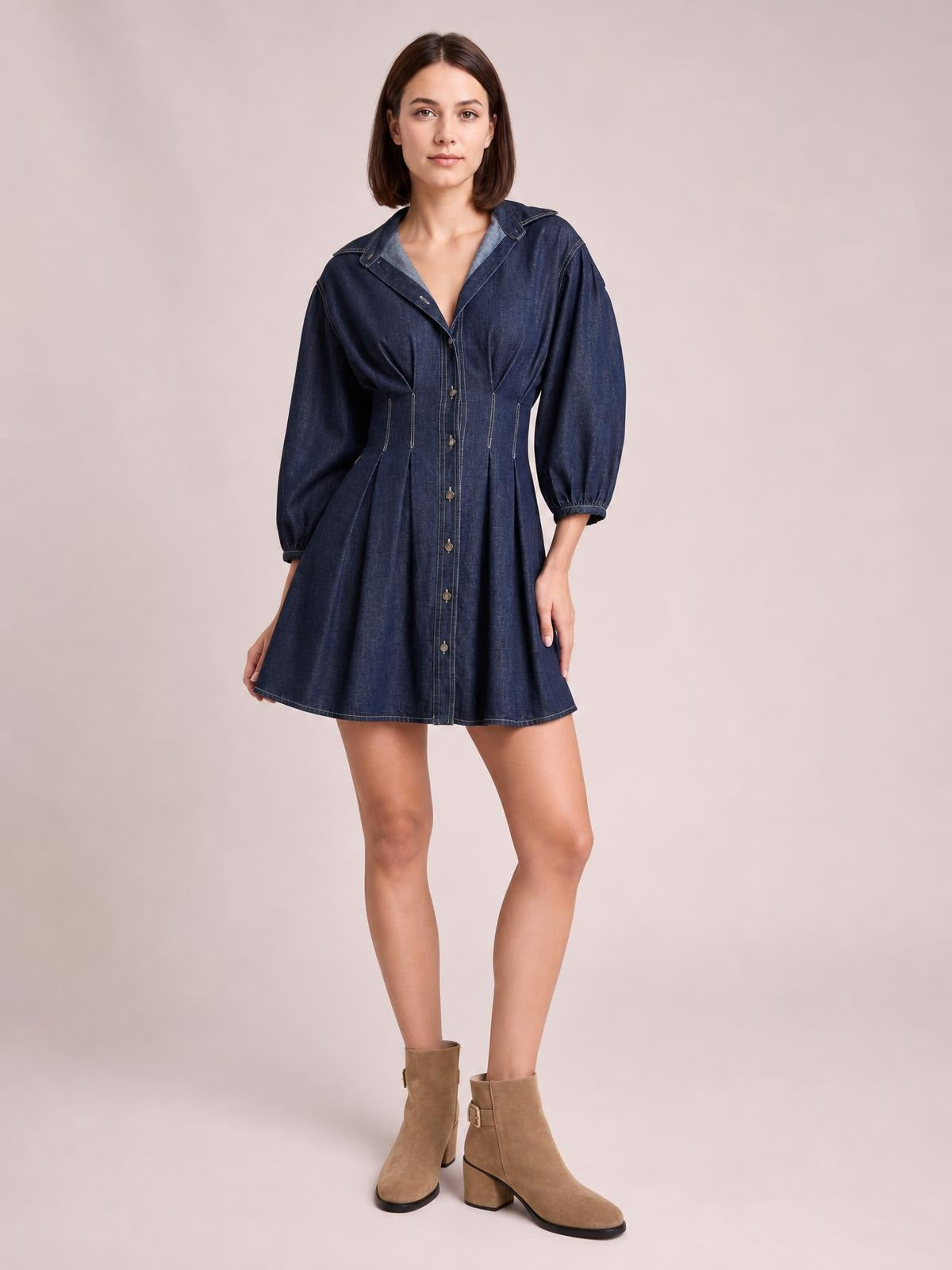 A model stands in a dark blue denim dress with button-down front, 3/4 sleeves, collar, seam detailing, fitted waist, and flared short silhouette.
