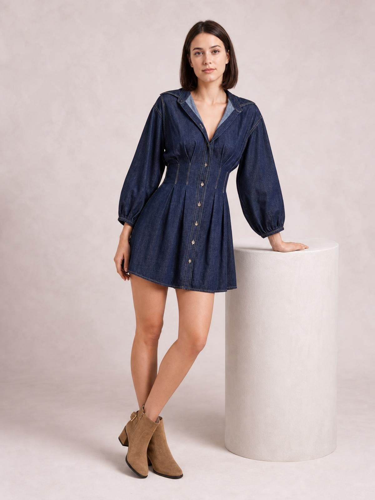 Model poses in a dark denim button-down dress with 3/4 balloon sleeves, contrast seam detailing, a fitted waist, and a flared short skirt.