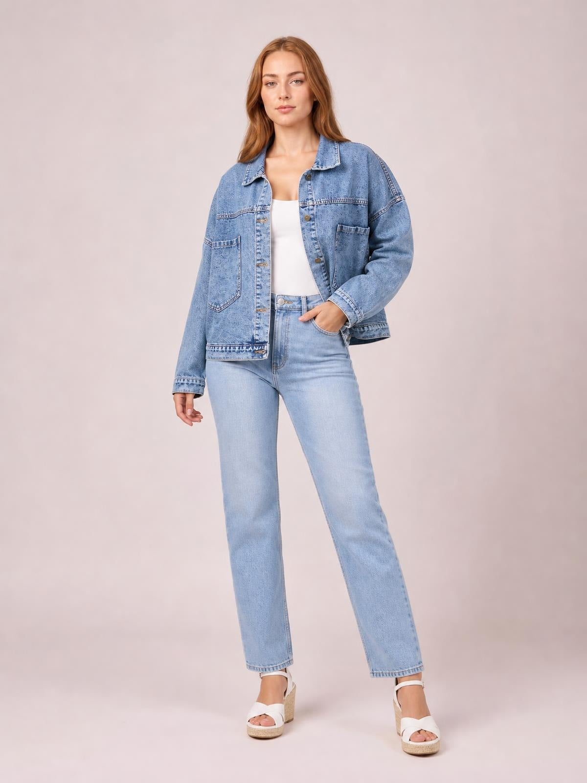 A model stands in a light blue button-down denim jacket shirt with drop shoulders, long sleeves, front pockets, and a relaxed silhouette.