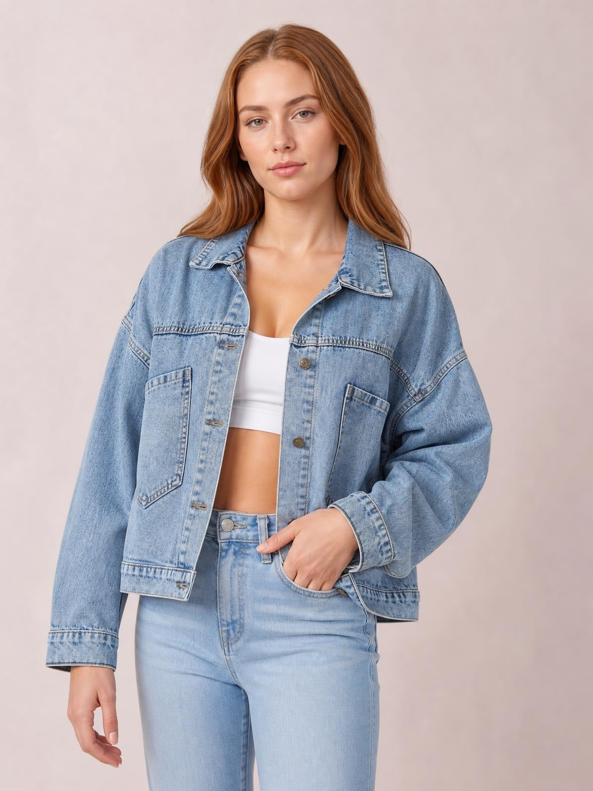 Model poses in a light blue button-down denim jacket with drop shoulders, a pointed collar, long sleeves, front buttons, and large patch pockets.