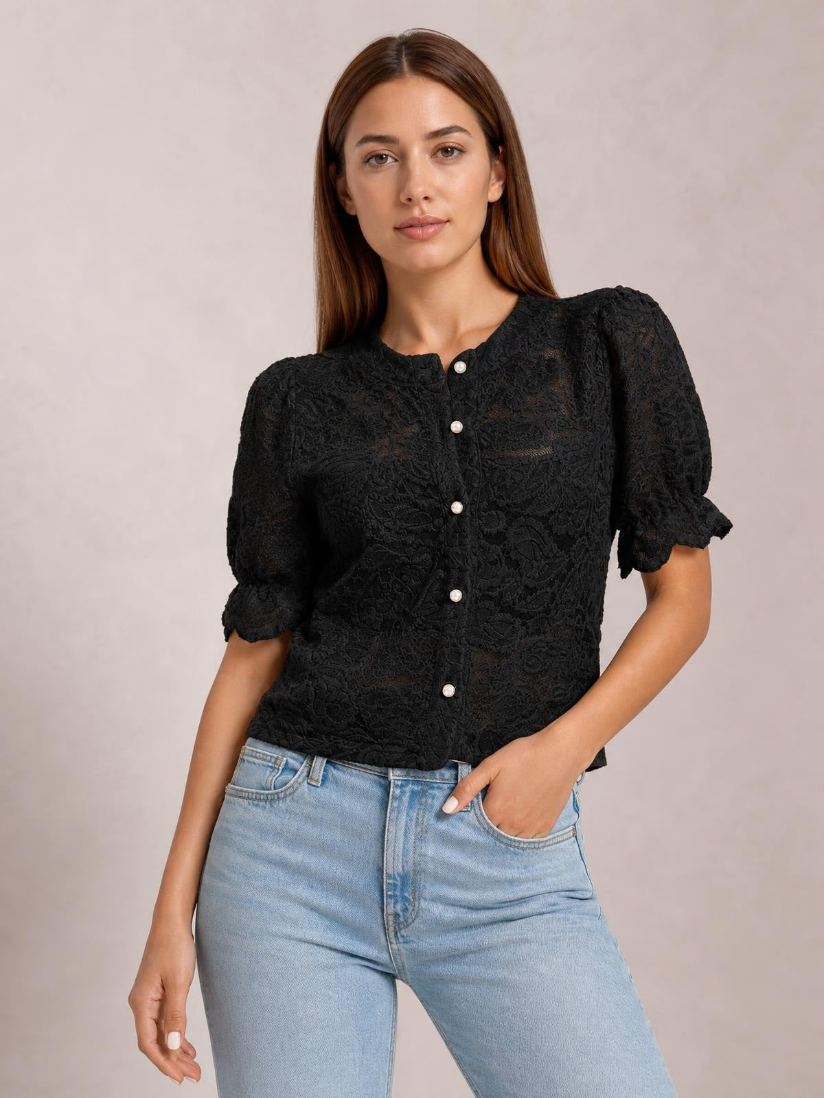 Model poses with one hand in her jeans pocket wearing a black sheer lace button-down shirt with a round neckline, half puff sleeves, and a relaxed silhouette.