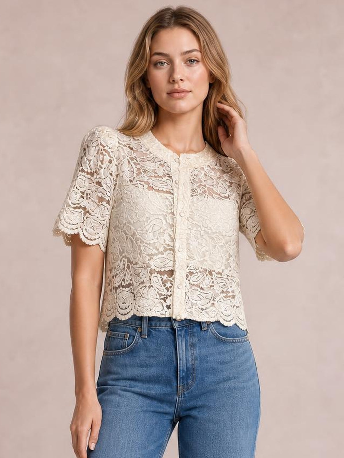 Model wearing a cream sheer lace button-down shirt with short scalloped sleeves and a relaxed cropped silhouette, posing with one hand near her hair.