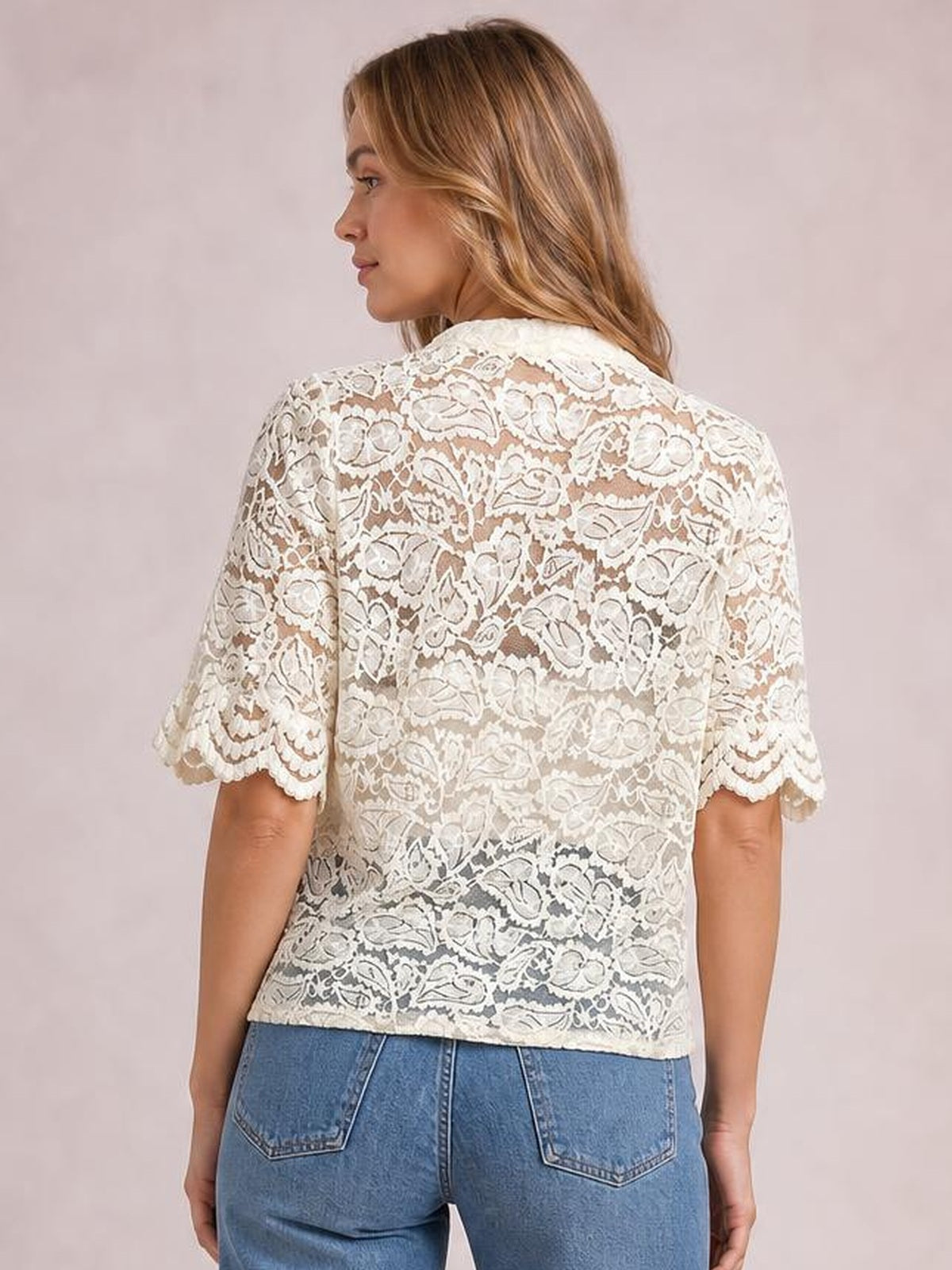 A model wears a sheer ivory floral lace shirt with half sleeves, scalloped cuffs, and a relaxed straight silhouette, viewed from the back.