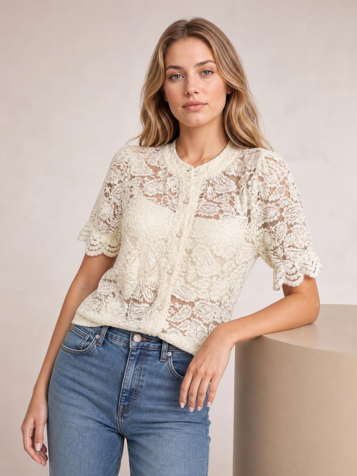 Model wearing an ivory sheer lace button-down shirt with a round neckline, front buttons, half sleeves, scalloped cuffs, and a relaxed silhouette.