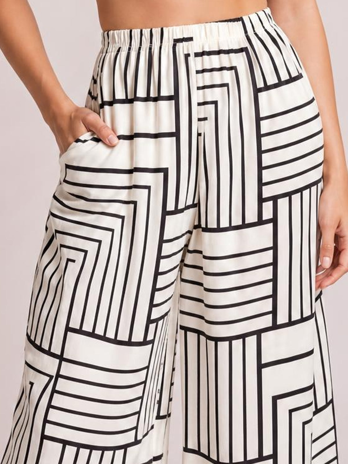 A model wears the white pants from a button-down top and pants set, featuring bold black geometric lines, a relaxed wide-leg silhouette, elastic waist, and pockets.