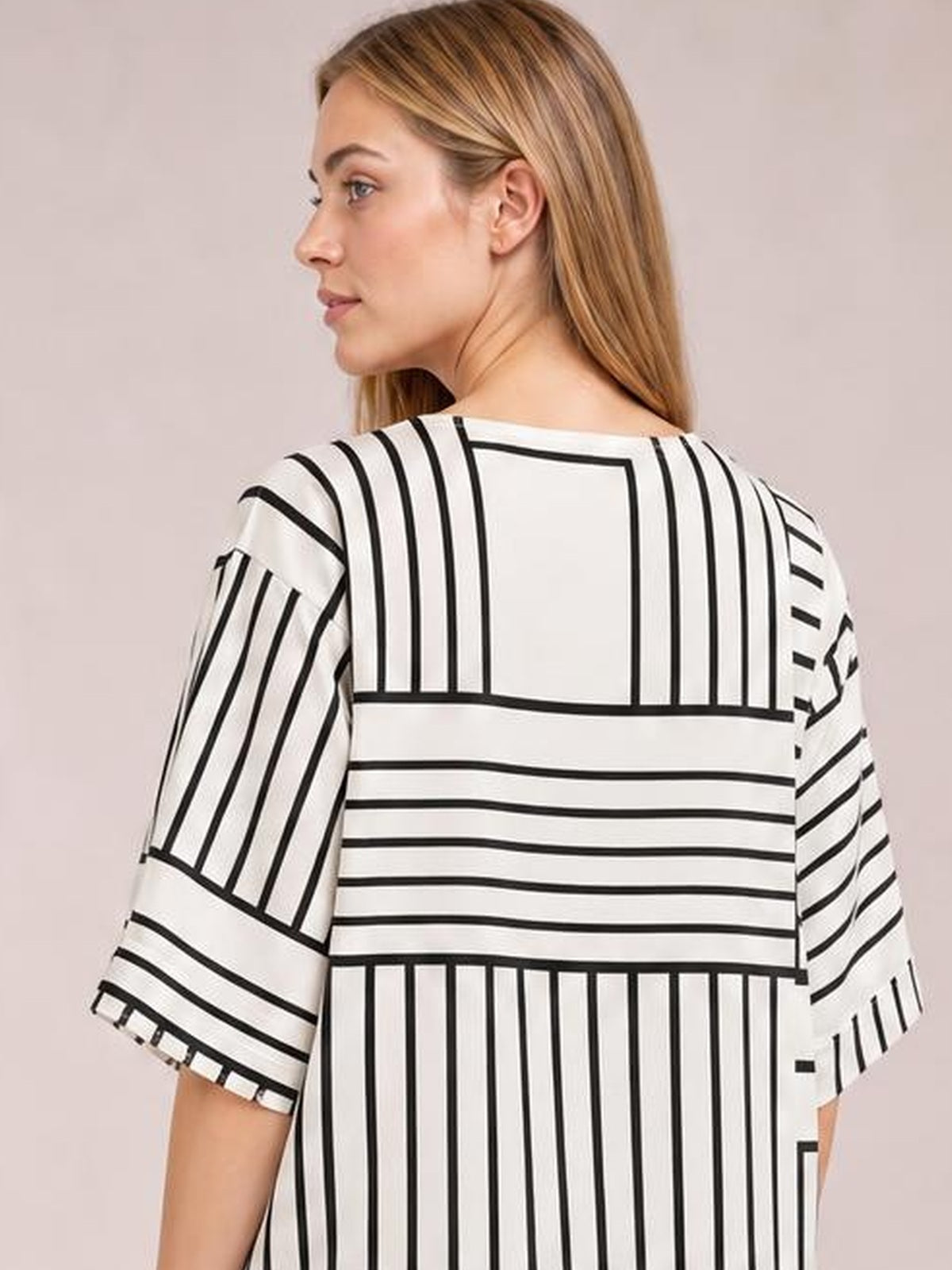 A model turns in profile to show the white half-sleeve top’s relaxed silhouette with bold black geometric stripes and contrasting vertical and horizontal panel construction.