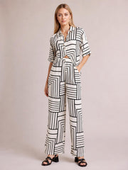 A model stands in a white geometric-print button-down half-sleeve top and matching pocketed wide-leg pants with a relaxed silhouette.