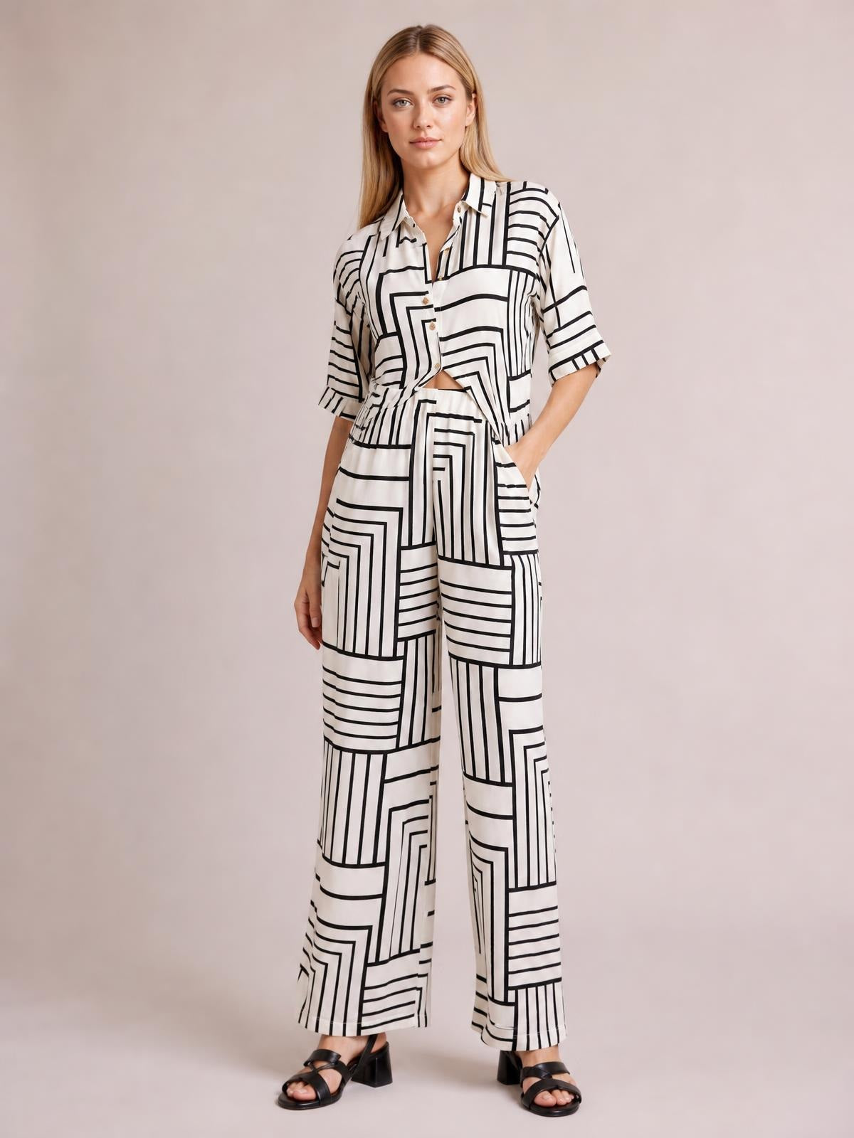 A model stands in a white geometric-print button-down half-sleeve top and matching pocketed wide-leg pants with a relaxed silhouette.