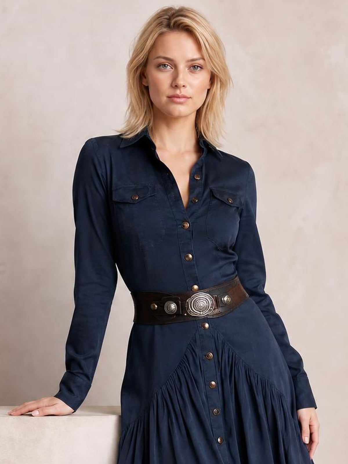 A model wears a navy button-down shirt dress with a collared neckline, long sleeves, flap chest pockets, front buttons, and gathered ruffle detailing.