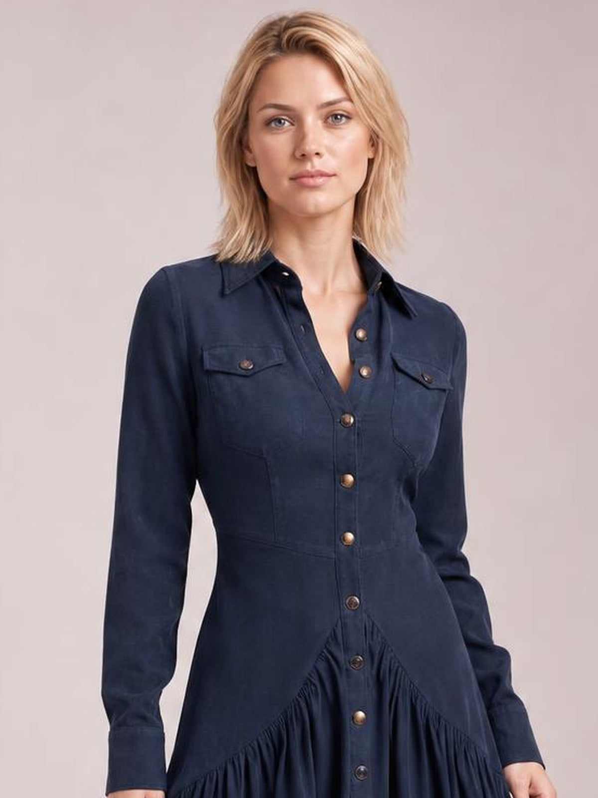 Model wears a navy button-down shirt dress with a pointed collar, long sleeves, flap chest pockets, fitted waist, and a ruffled high-low hem.