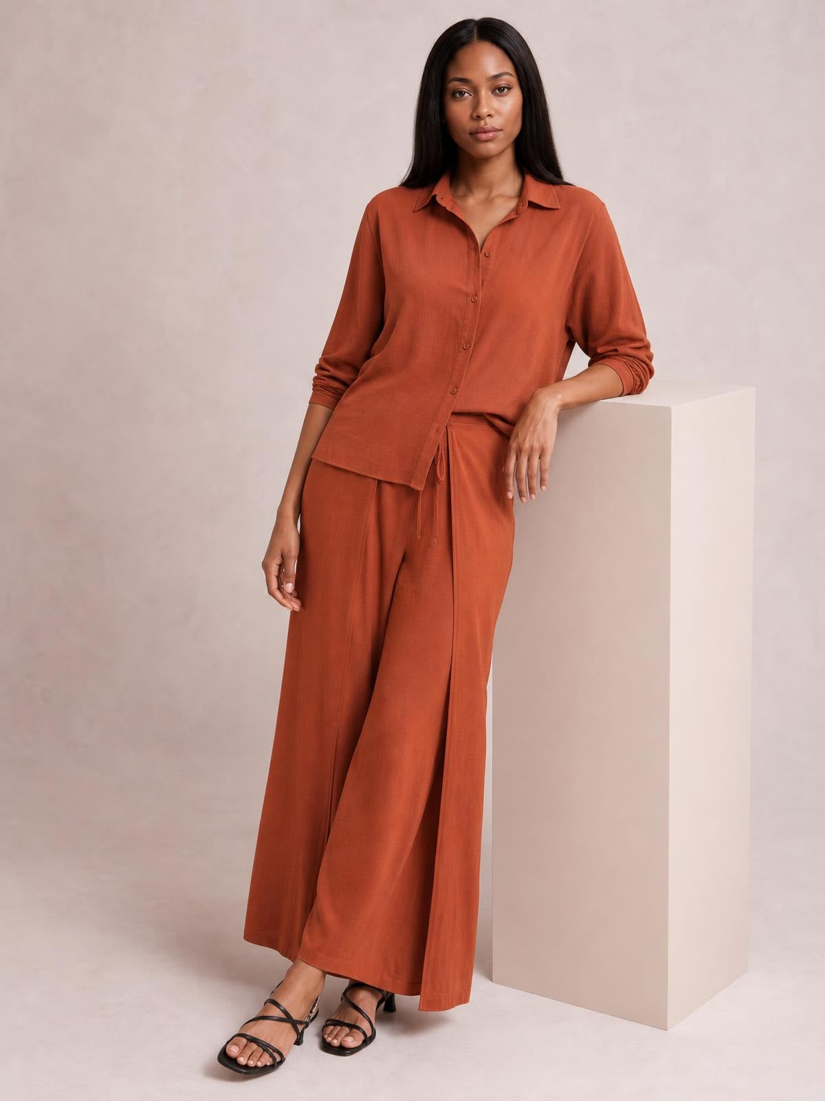 Model stands in a rust-orange button-down long-sleeve top and matching drawstring wide-leg pants, showing a relaxed, fluid silhouette.