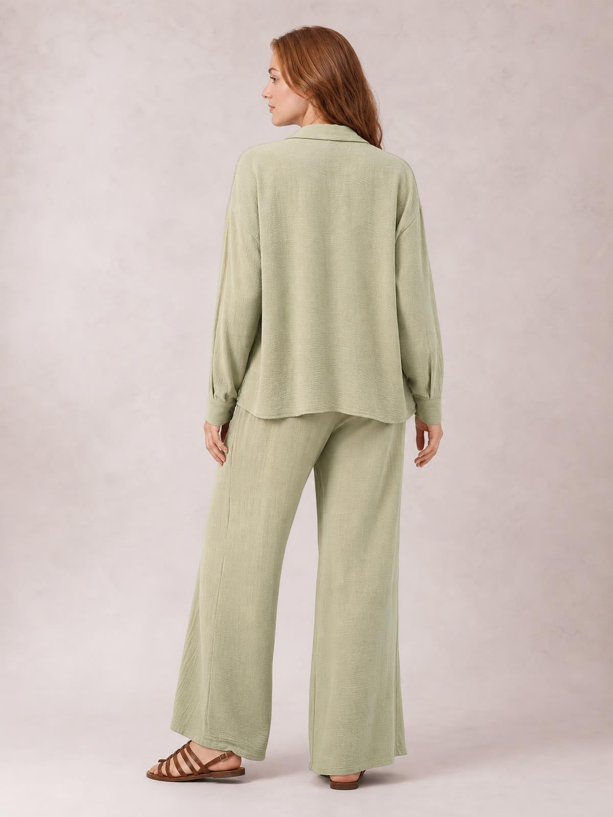 A model stands turned away in a sage green long-sleeve button-down top with a relaxed silhouette and matching fluid wide-leg pants.