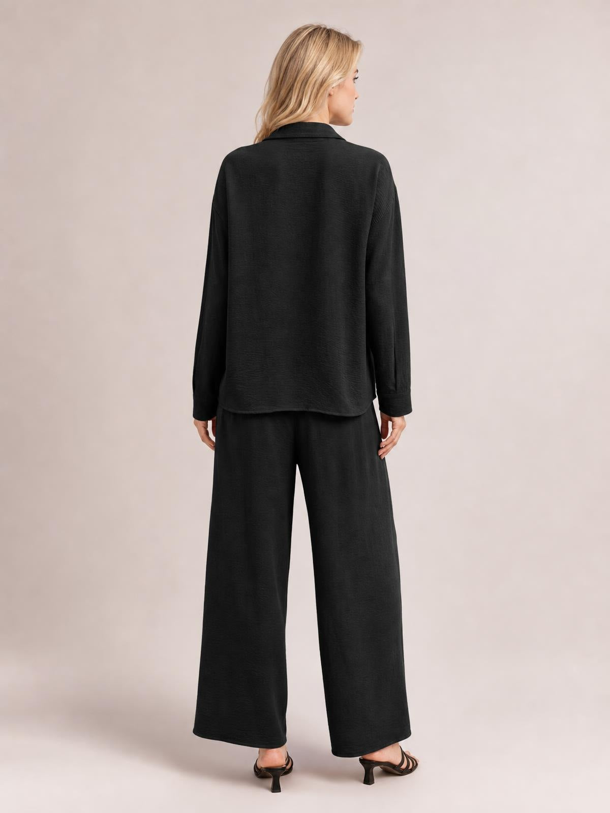 Model shown from the back in a black button-down long-sleeve top and relaxed wide-leg pants set, featuring a collared shirt and fluid silhouette.