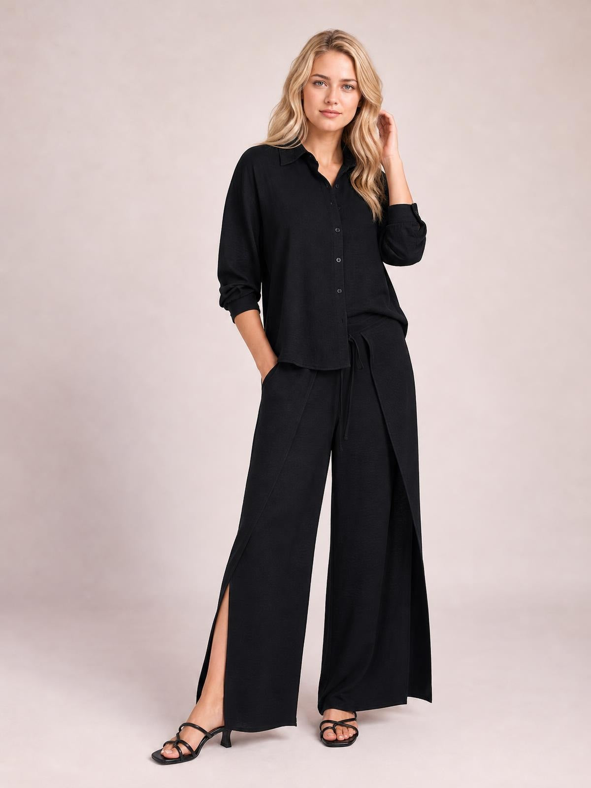 Model in a black button-down long-sleeve top and wide-leg pants set, posed with one hand in a pocket, drawstring waist, and slit accents.