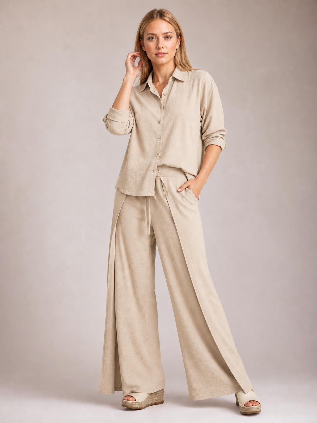 A model poses in a beige button-down long-sleeve top and wide-leg pants set, featuring a relaxed silhouette, drawstring waist, and side slit accents.