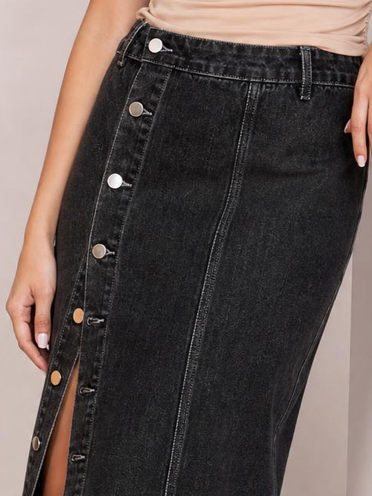 A model wears a black denim midi skirt with a fitted silhouette, high waistband, contrasting stitching, and a button-down front opening into a side slit.