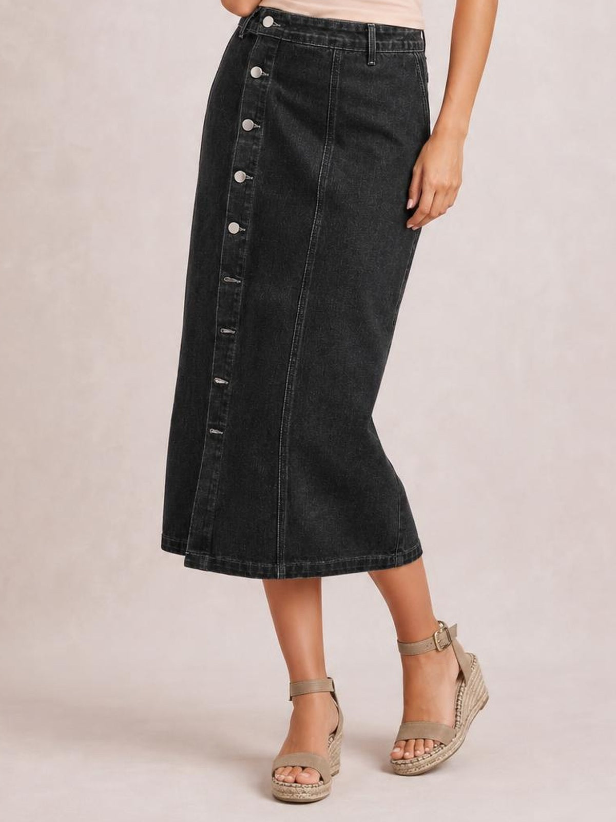 A model poses in a black denim midi skirt with a high waist, fitted straight silhouette, front button-down closure, and contrast stitching.