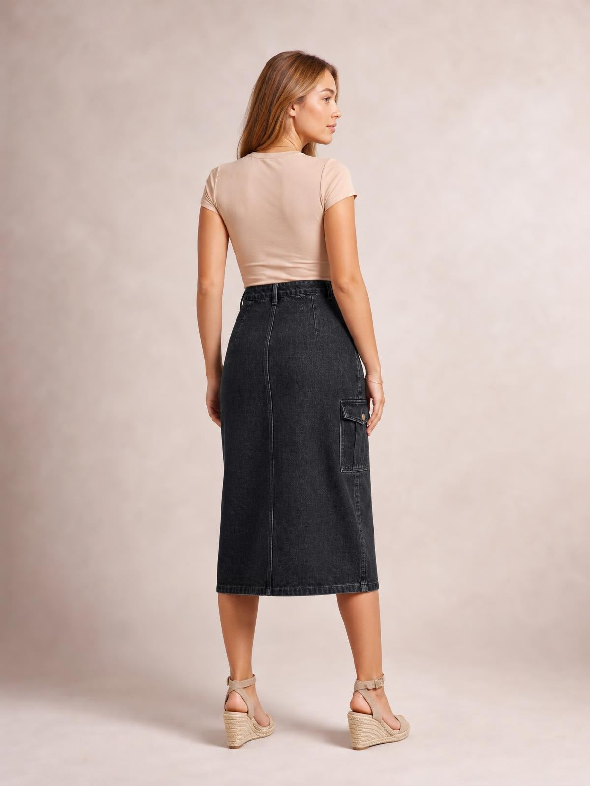 A model stands turned away in a dark denim midi skirt with a straight silhouette, defined waistband, visible seams, and a large flap pocket.