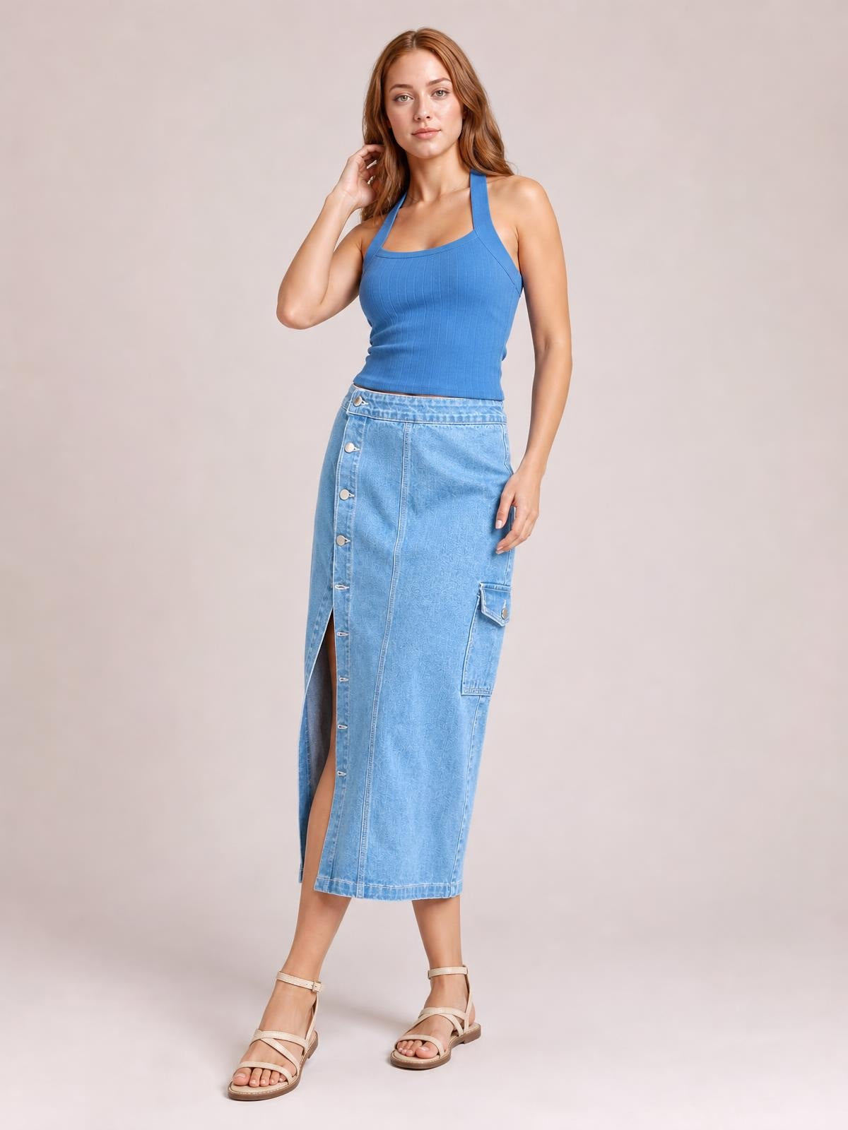 Model poses in a light blue denim midi skirt with a straight silhouette, button-down front, side cargo pocket, and front slit.