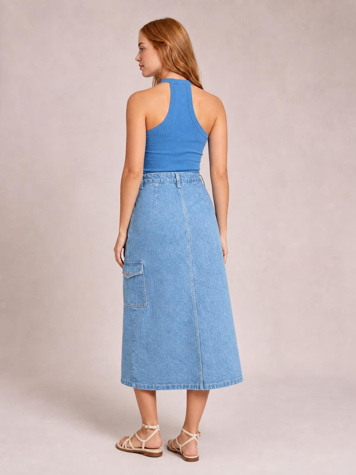 Model shown from behind in a light blue denim midi skirt with a straight silhouette, waistband, belt loops, center seam, and large patch pocket.