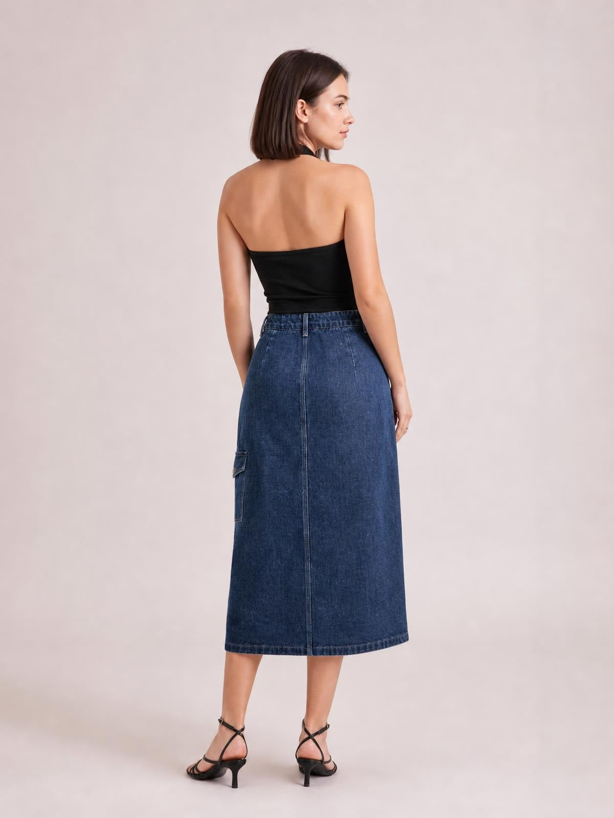 Model shown from behind wearing a dark blue button-down midi denim skirt with a high waist, straight silhouette, center seam, and side pocket.