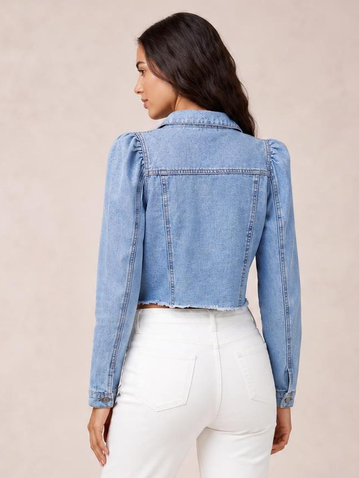Model shown from behind wears a light-blue button-down cropped denim jacket with long sleeves, structured seams, and a visibly raw hem.