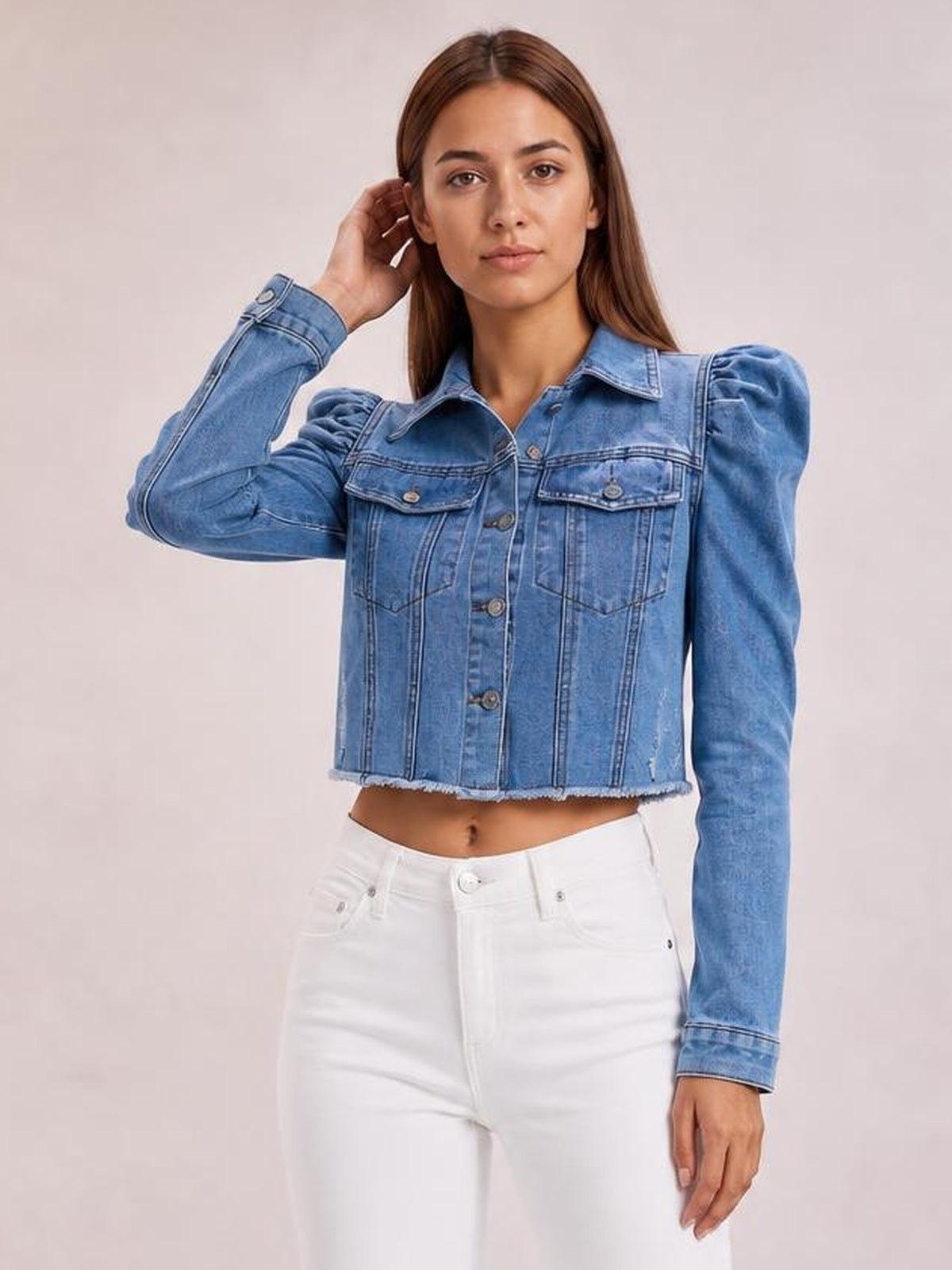 Model poses in a light blue button-down cropped denim jacket with puff sleeves, chest pockets, front buttons, structured seams, and a raw hem.