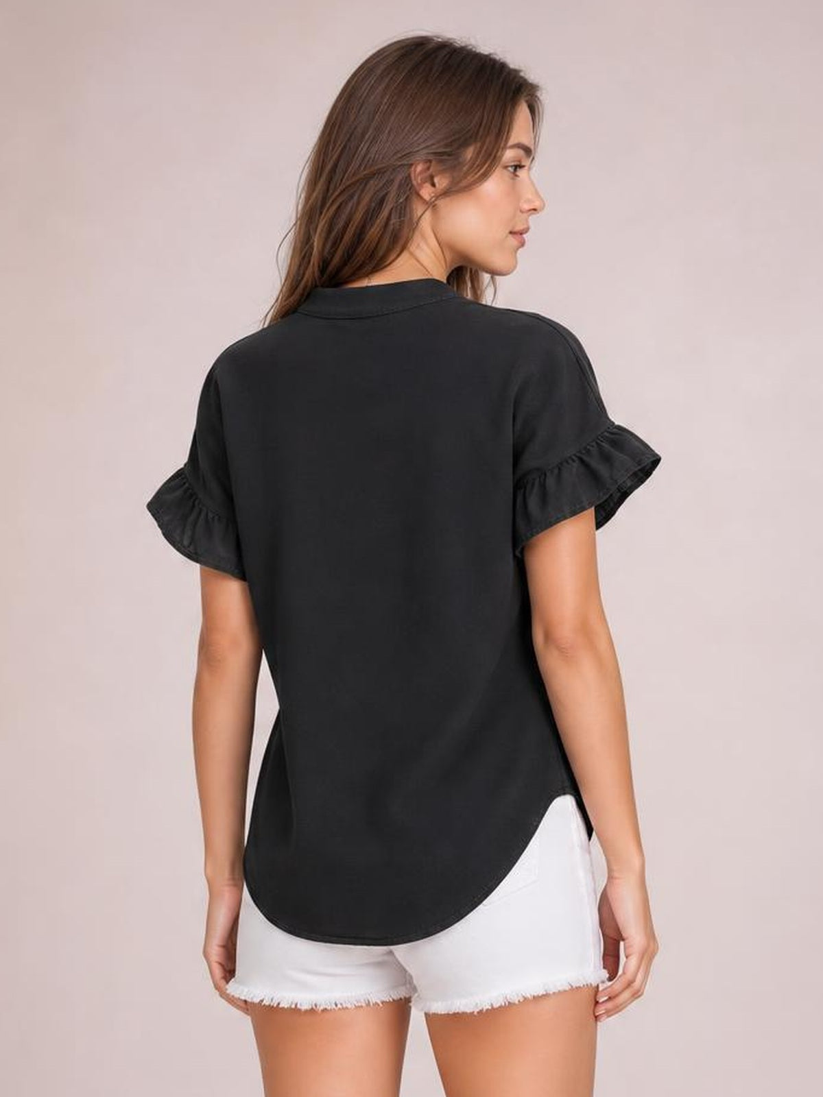 A model looks over her shoulder in a black opaque short-sleeve shirt with ruffled sleeves, a relaxed silhouette, and a curved hem.