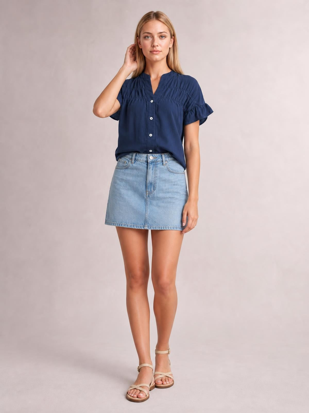 A model stands in a navy button-down shirt with ruched detailing, a split neckline, short ruffled sleeves, and a relaxed silhouette.