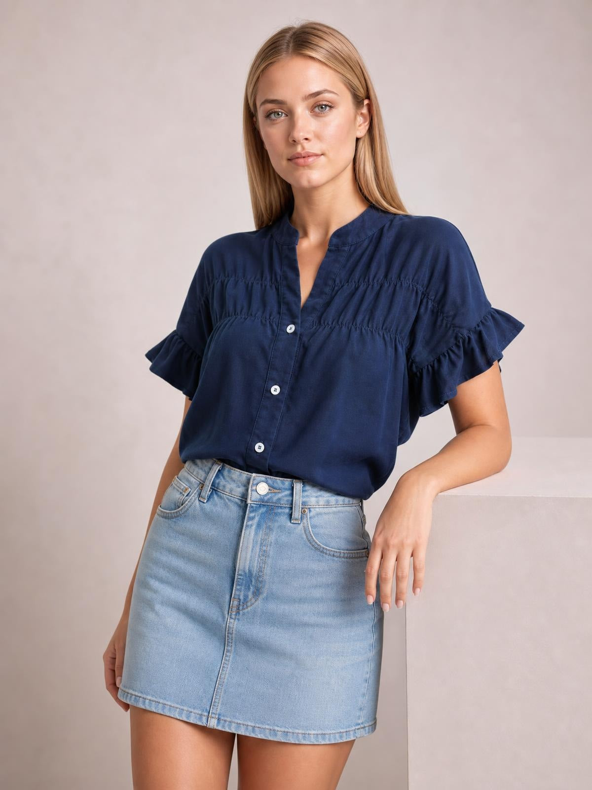 Model poses in a navy button-down shirt with short ruffled sleeves, ruched seams, a gently relaxed silhouette, and visible front buttons.