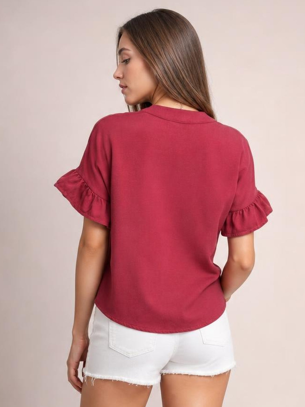 A model turned away wears a burgundy button-down shirt with a relaxed silhouette, short sleeves, and gathered ruffled cuffs.
