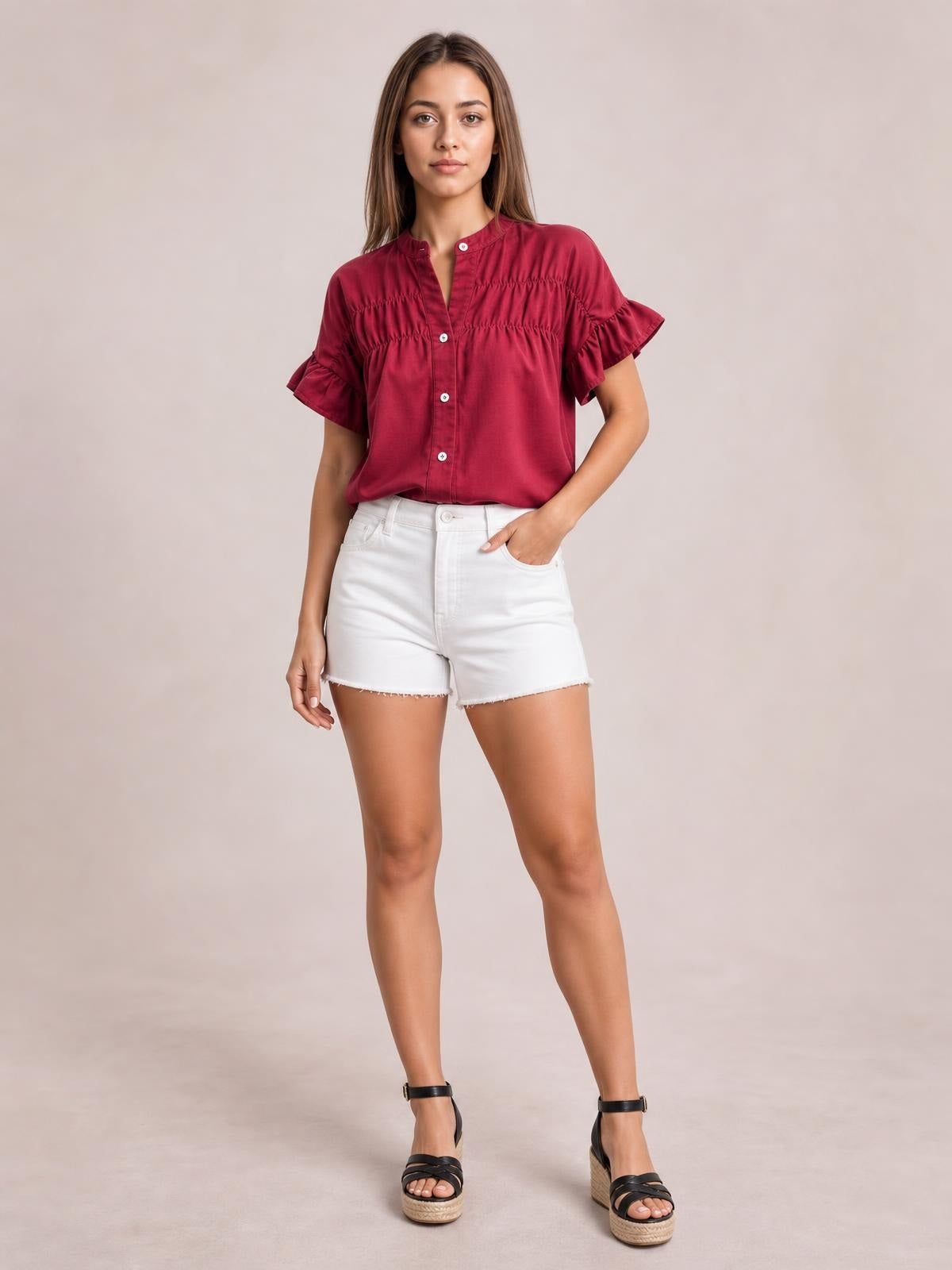 Model wears a burgundy button-down shirt with short ruffled sleeves, ruched detailing, a relaxed silhouette, and a hand resting in her pocket.