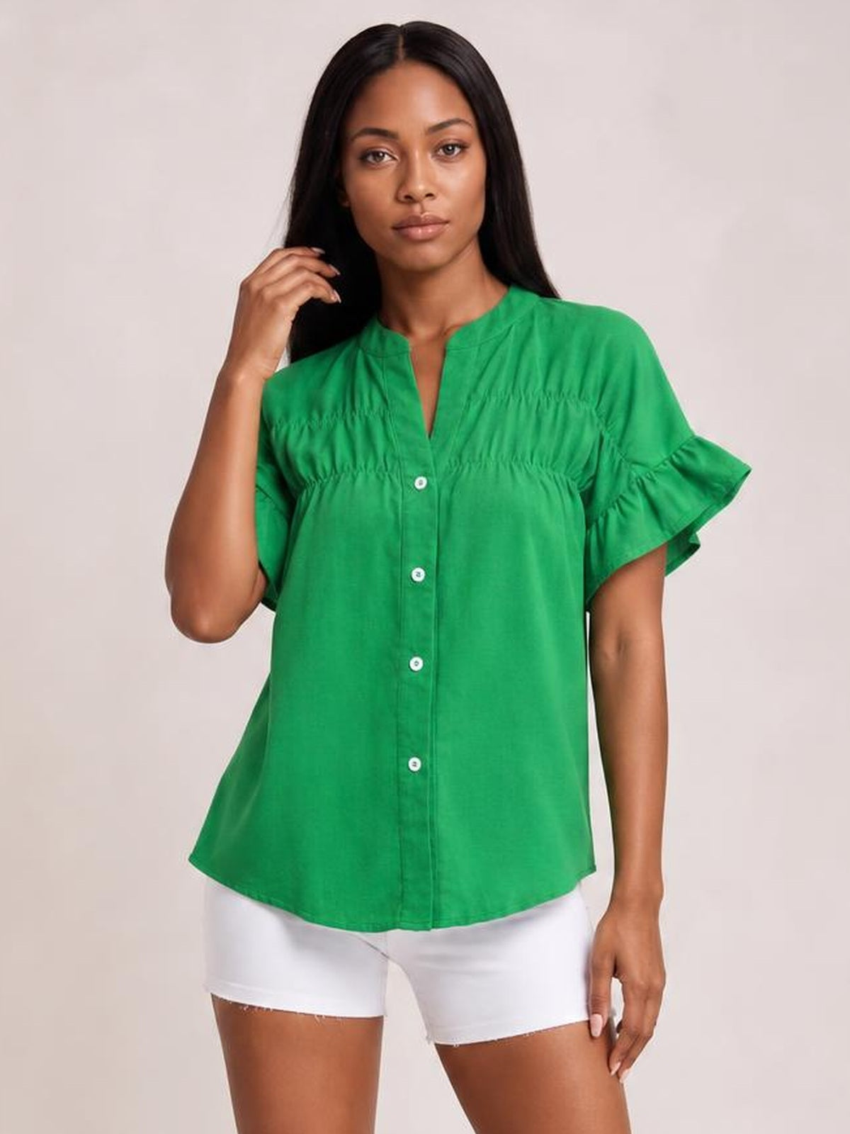 Model poses in a green button-down shirt with a relaxed silhouette, ruched detailing, and layered ruffled short sleeves.