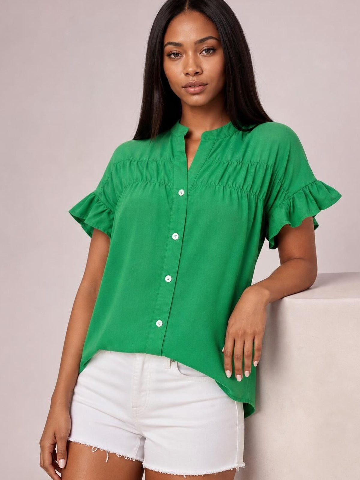 Model wears a bright green button-down shirt with ruched seams, a relaxed silhouette, and layered ruffled short sleeves while leaning casually.