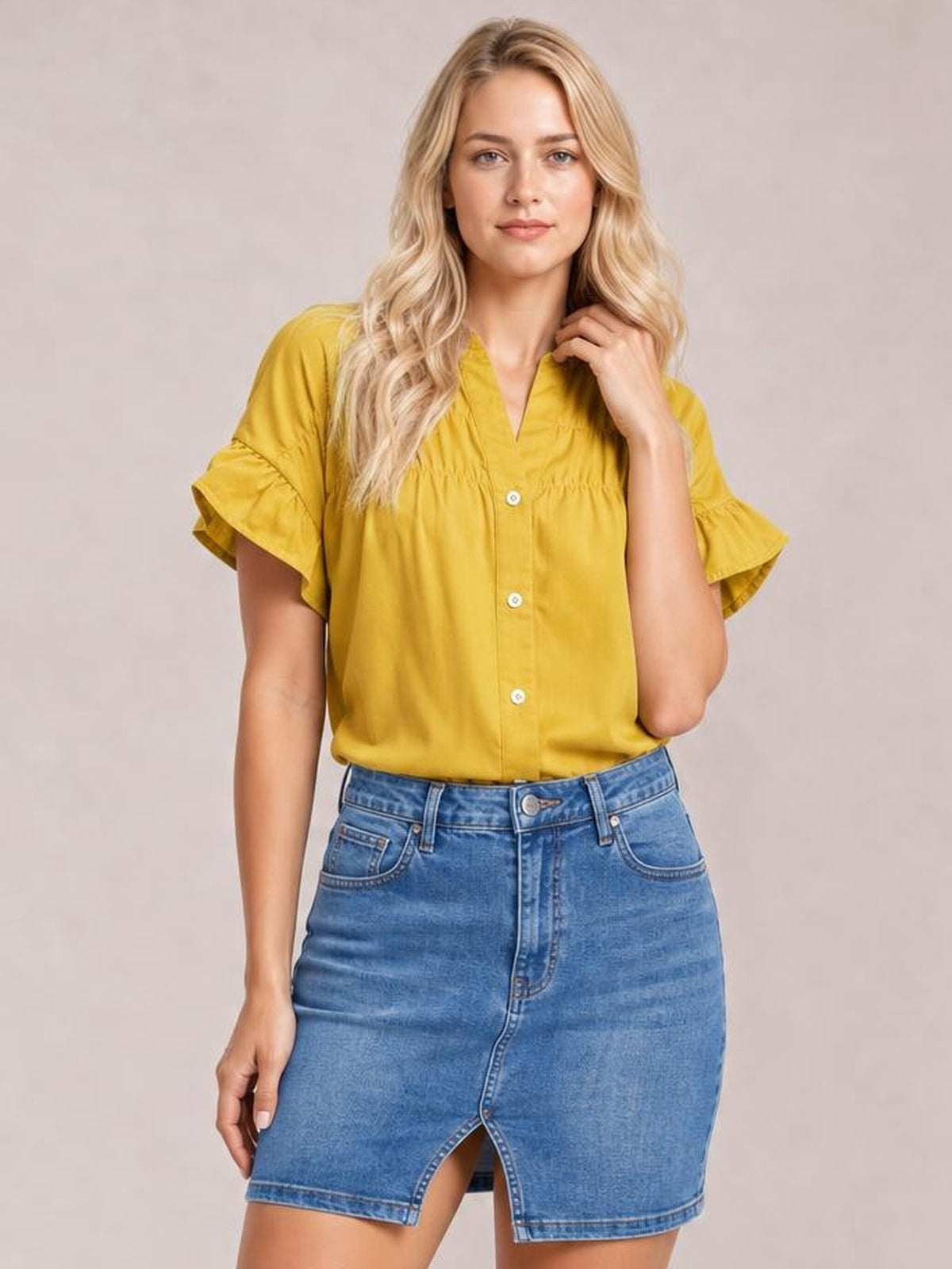 A model poses in a mustard-yellow button-down shirt with ruched detailing, a relaxed silhouette, and feminine ruffled short sleeves.