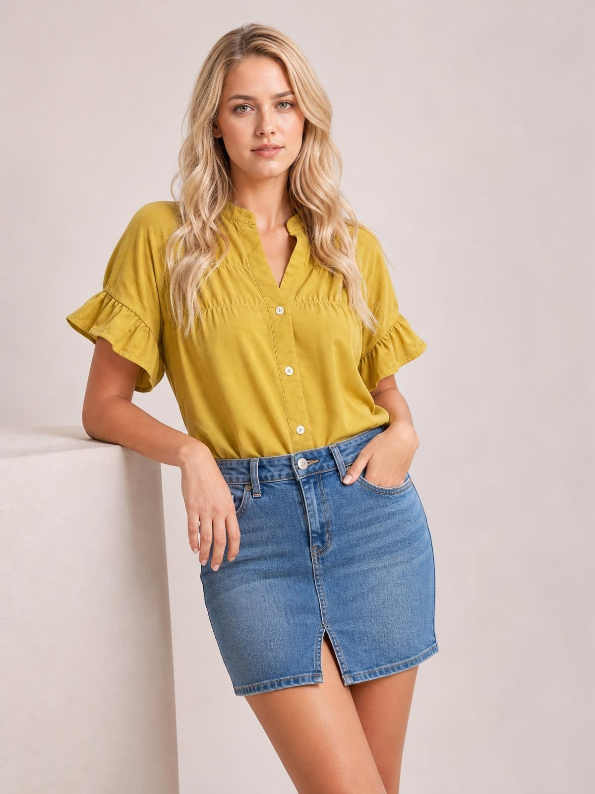 A model poses in a mustard-yellow button-down shirt with a relaxed silhouette, ruched front, and feminine ruffled short sleeves.
